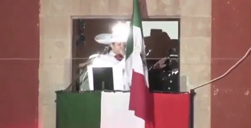 Betty Hernández tosiendo en el palco dando el grito.